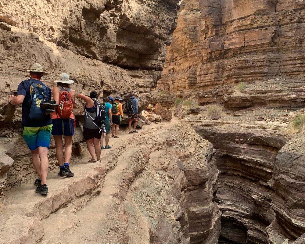 Hiking along a narrow ledge through Deer Creek Canyon to reach The Patio oasis above the Colorado River in Grand Canyon