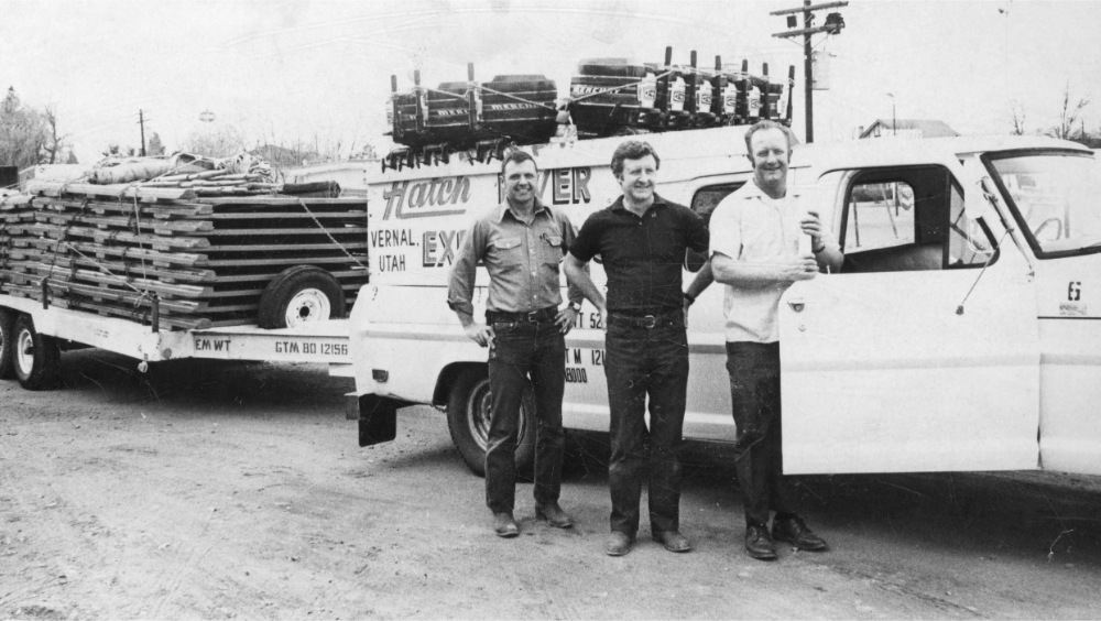 black and white photo of three men (including Don and Ted Hatch) in the 1960s next to the Hatch River Expeditions truck and trailer