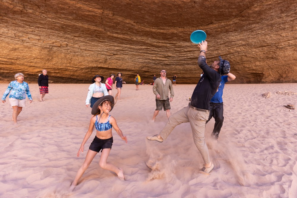 group of people play frisbee on the red sand in redwall cavern in grand canyon
