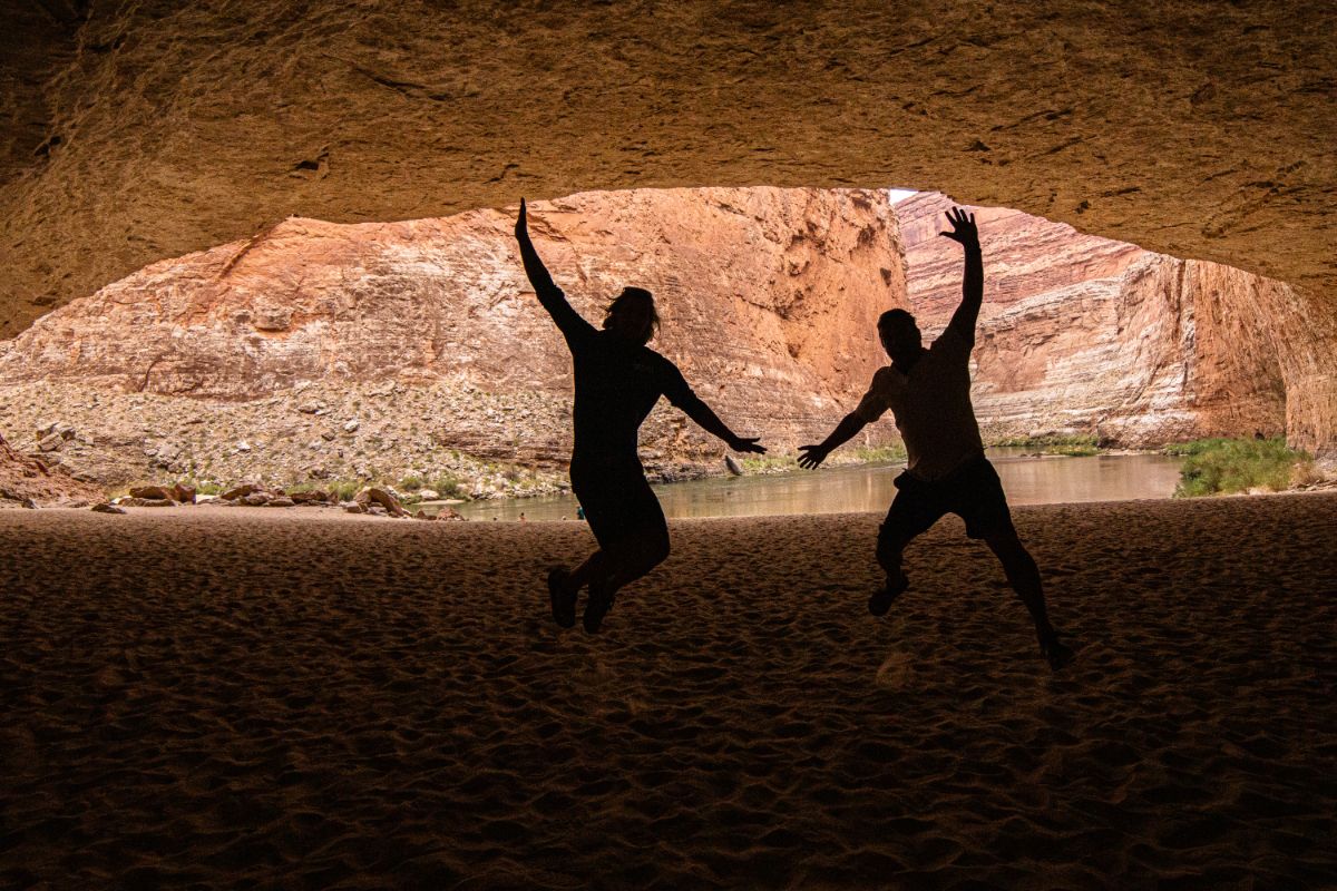 two people jump in the sandy Redwall Cavern in Grand Canyon