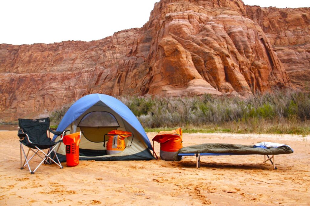 a photo of a sandy beach in Grand Canyon displaying all the included camping gear for a rafting trip including, tent, camp chair, dry bags, cot, sleeping bag, and pillow