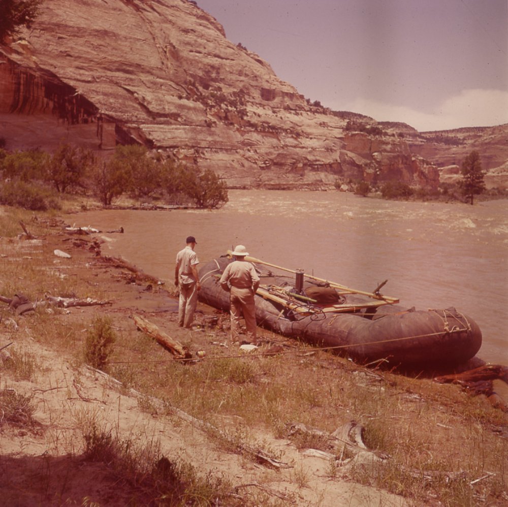 two men look at a military surplus pontoon repurposed as a river raft in the 1950s
