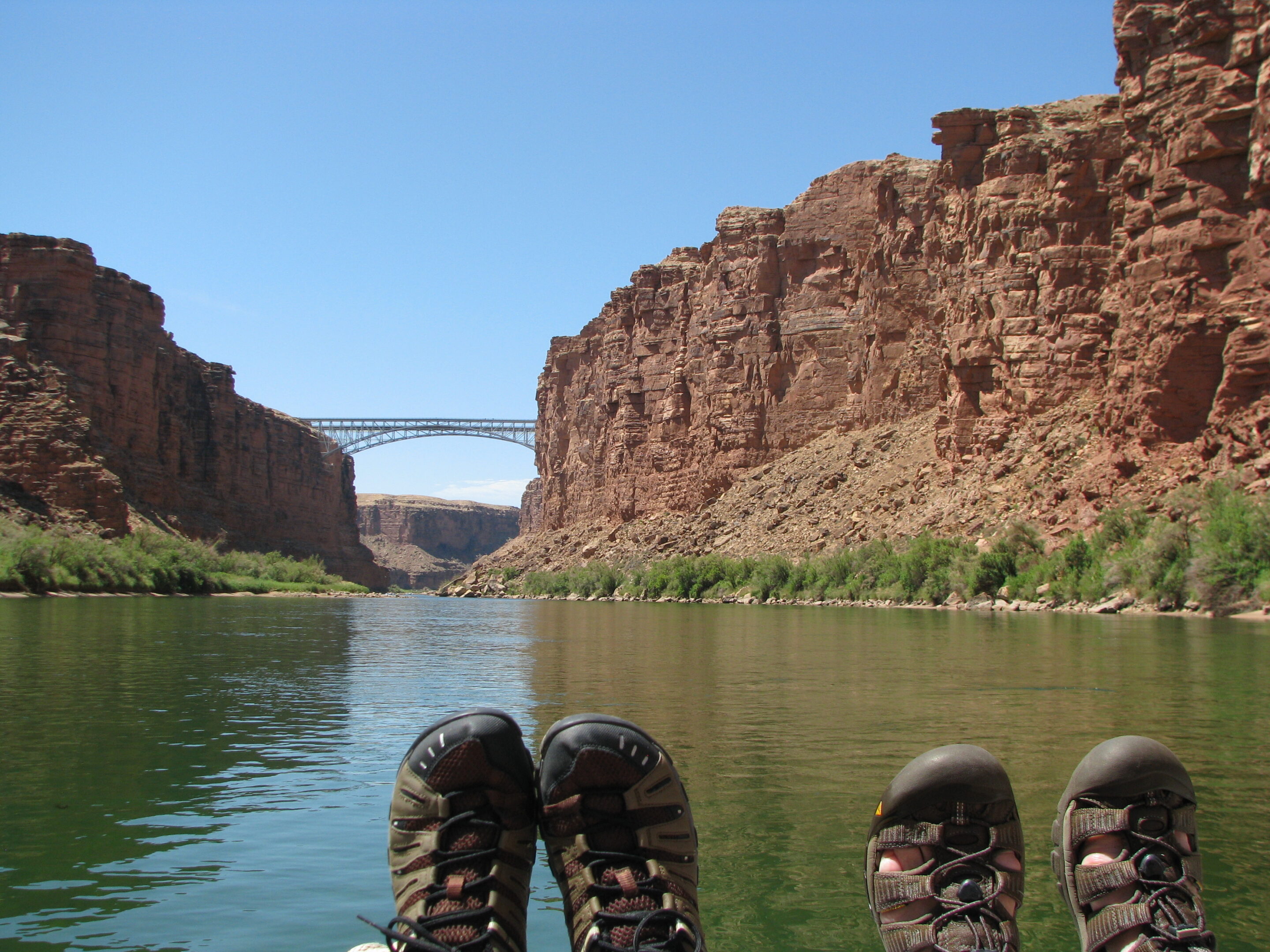 Two pairs of feet in Keen sandals on the front of a raft with Grand Canyon in the background. Photo credit: David Miller.