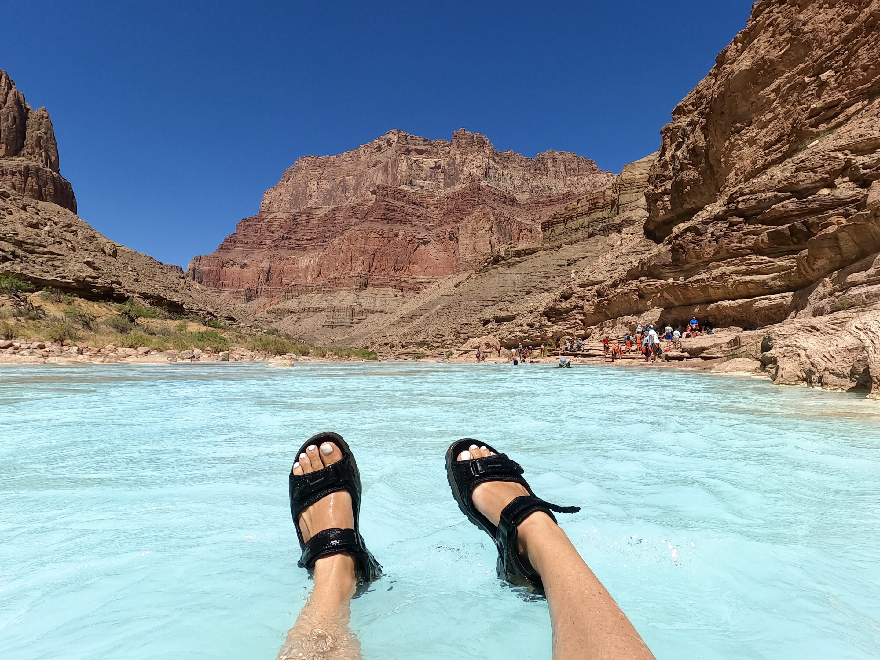 Feet in Teva sandals floating in the bright blue Little Colorado River in Grand Canyon