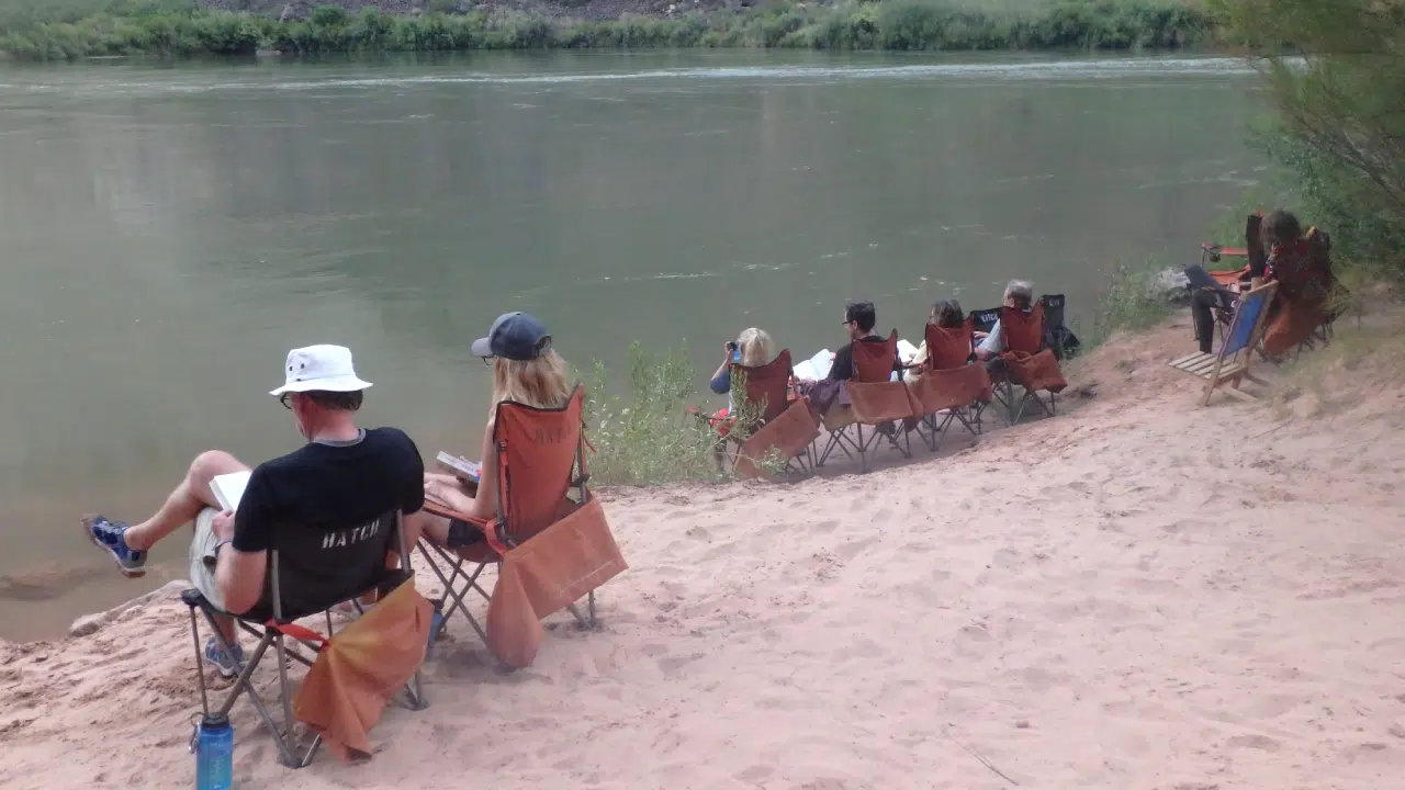 People sitting in chairs along colorado river on upper grand canyon expedition