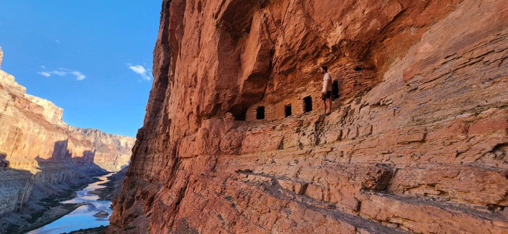 Man stands in front of Nankoweap Graneries with view of Colorado River to the left