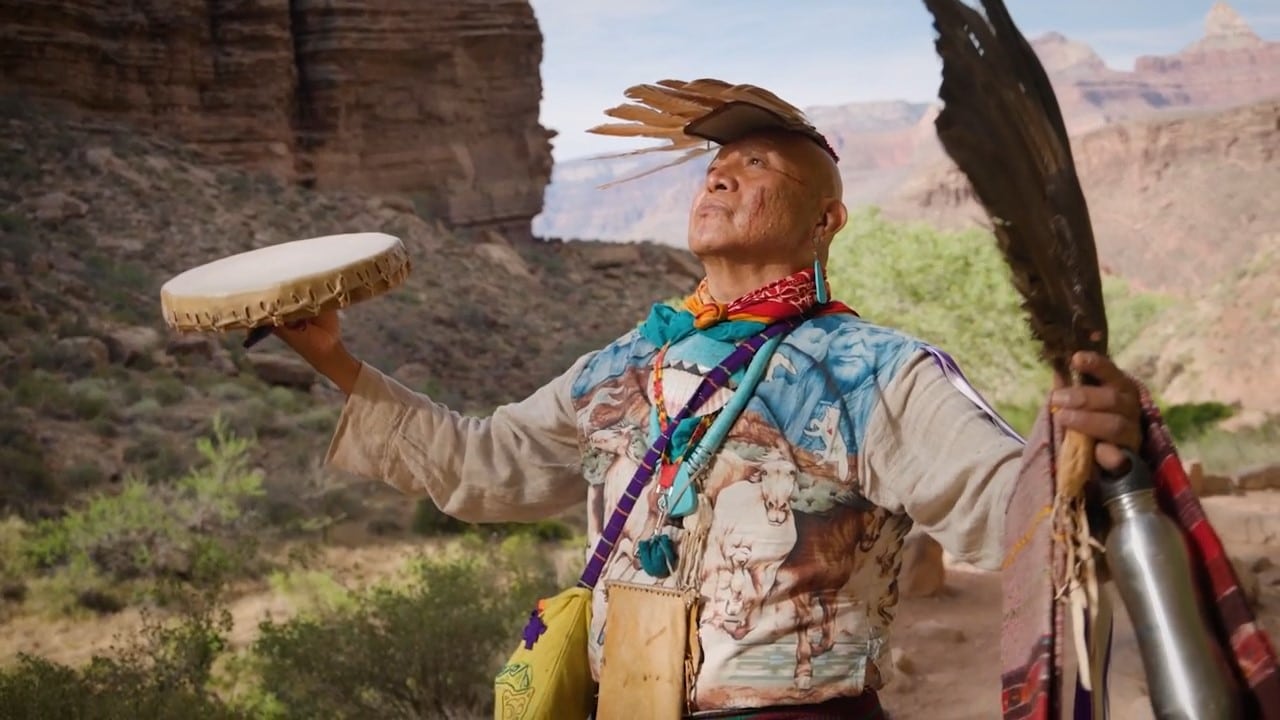 Screenshot from "We Are Grand Canyon" film from Grand Canyon Conservancy and the Intertribal Working Group. Image depicts a Native American man wearing and holding ceremonial items necessary for a blessing ceremony.