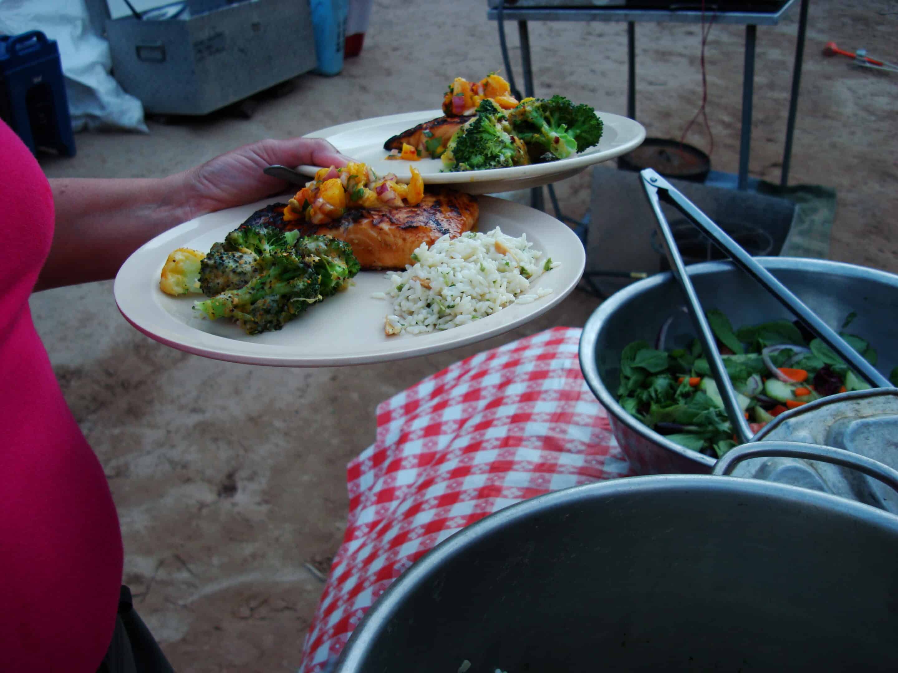 Person holding two plates and loading them up with chicken, rice, and broccoli.