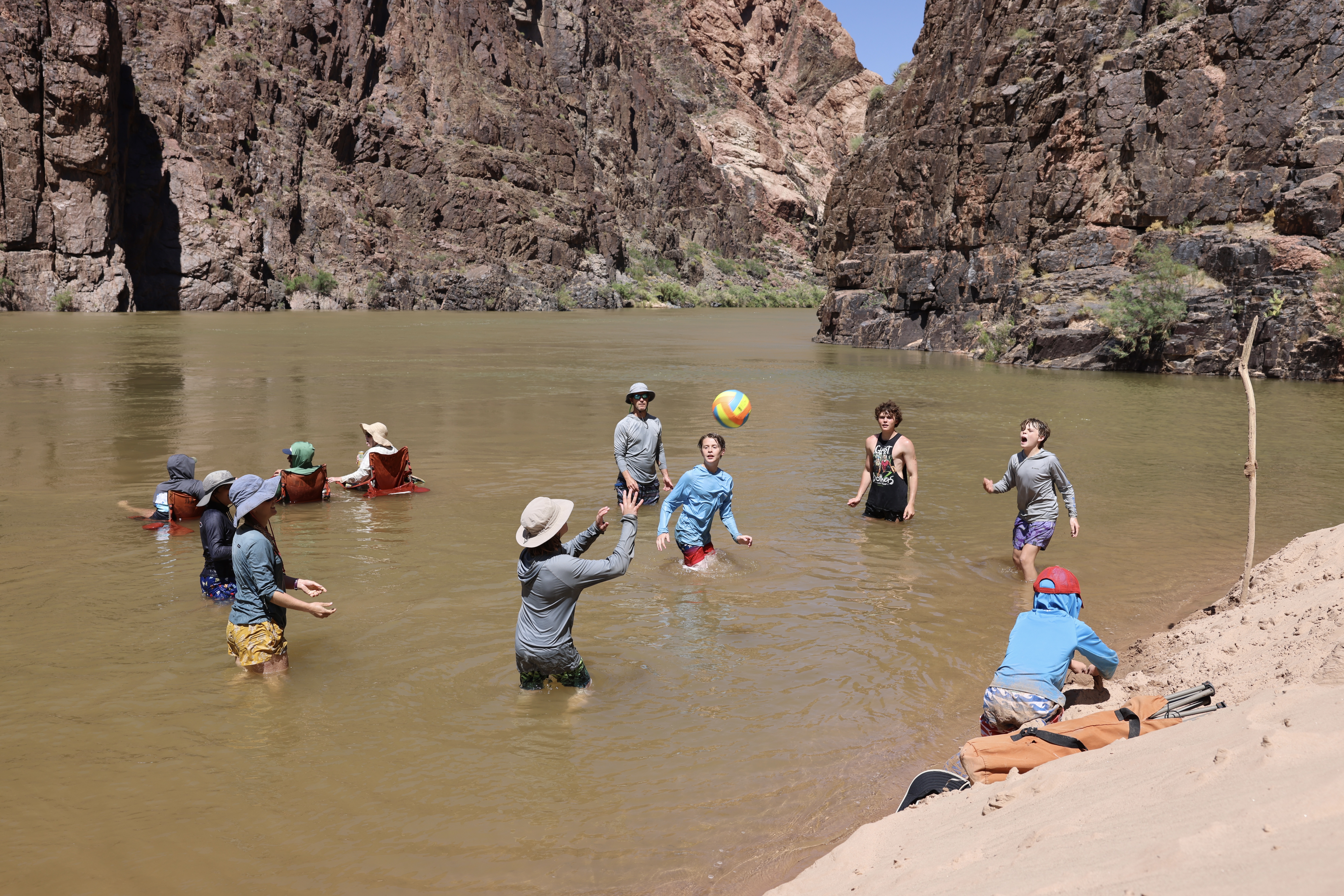 Kids playing volleyball in the Colorado River in Grand Canyon while other people sit in camping chairs in the river to cool off. 4 types of people you'll meet on a Grand Canyon river trip with Hatch River Expeditions.