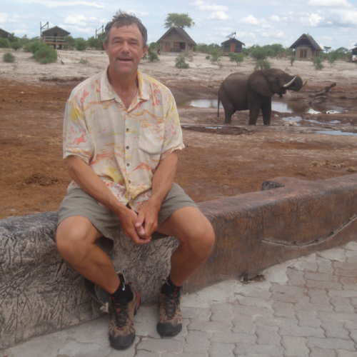 Guide from Hatch River Expeditions sitting near a waterhole with an elephant in the background.