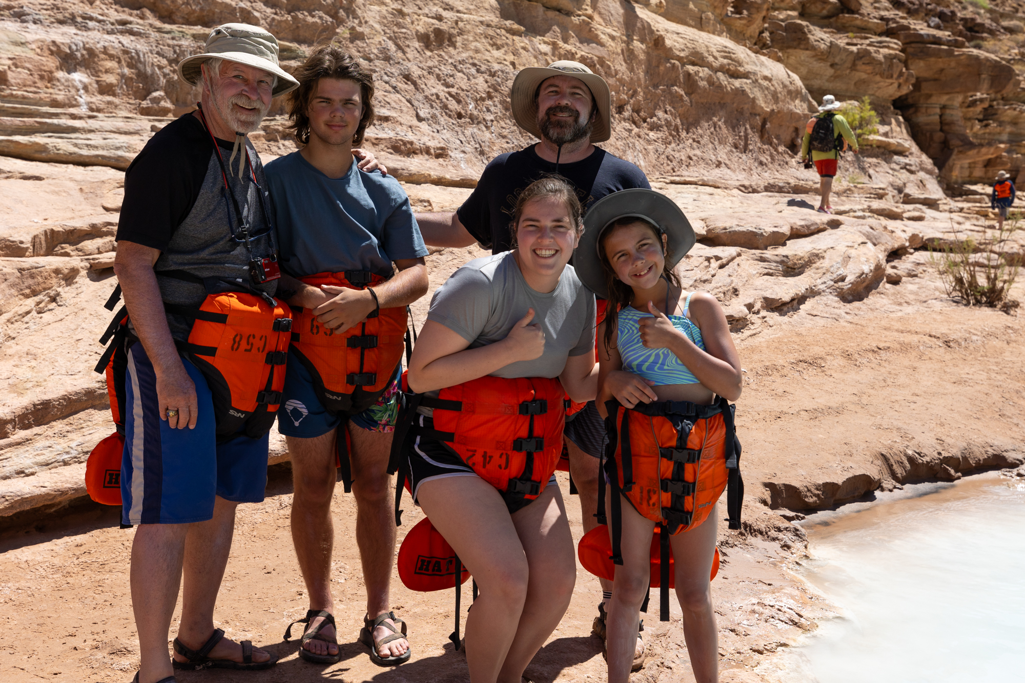 A multi-generational family poses for a photo beside the Little Colorado River. All are wearing their lifejackets around their waists in order to play in the river. Photo credit: Megan Ford Fyffee. 