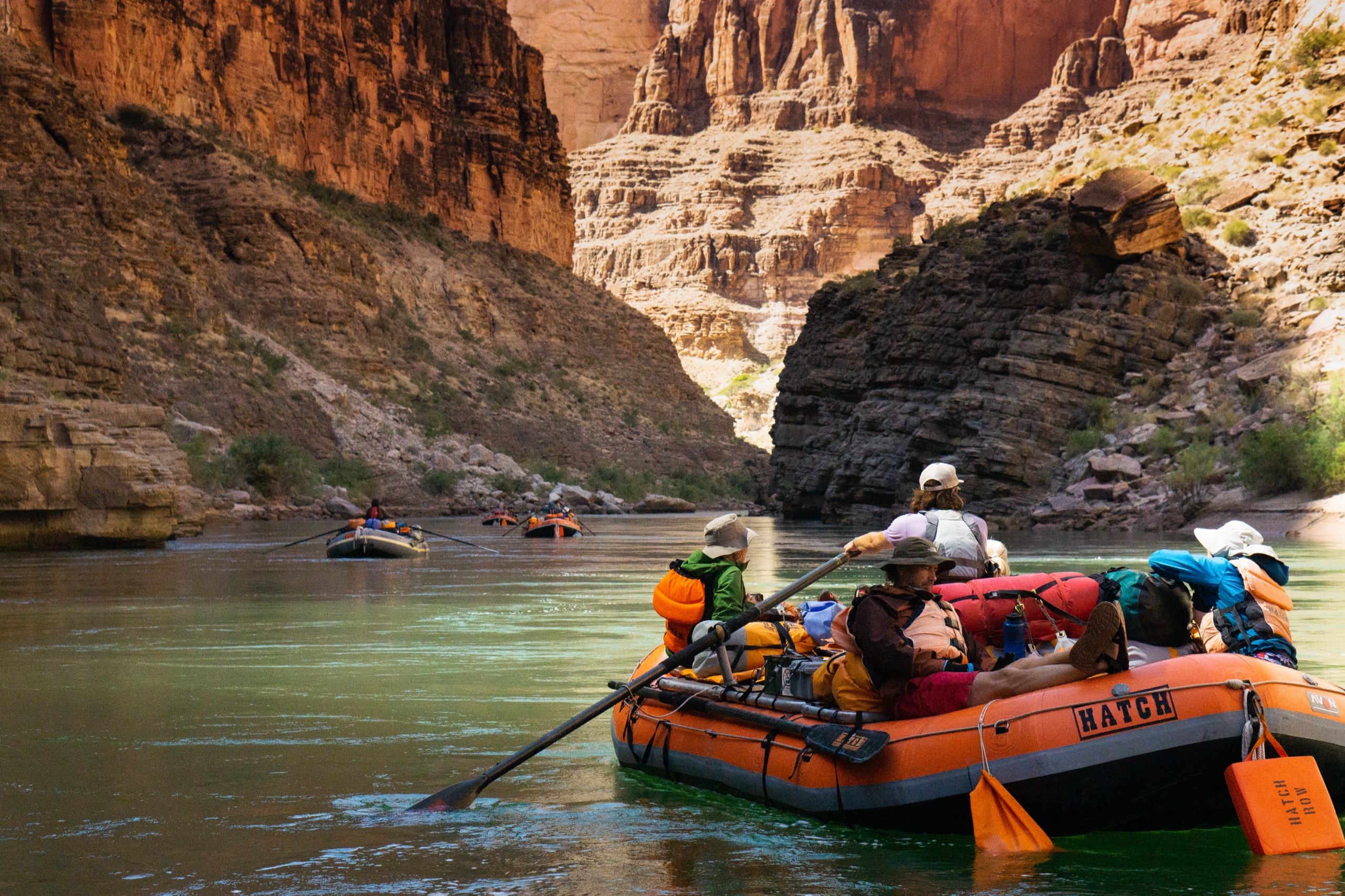 A Hatch guide rowing an orange oar raft of guests down the Colorado River, with more rafts ahead